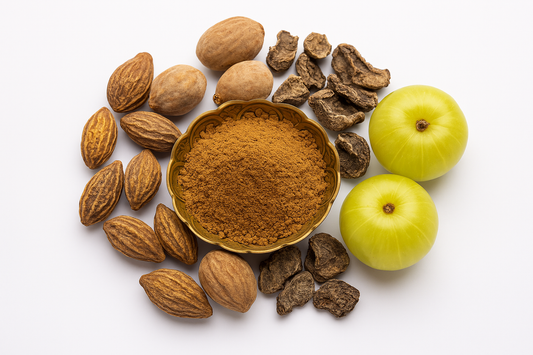 Triphala powder in a decorative brass bowl surrounded by dried haritaki, bibhitaki, and fresh amla fruits on a white background – showcasing Ayurvedic ingredients used for digestion, detox, and immunity.